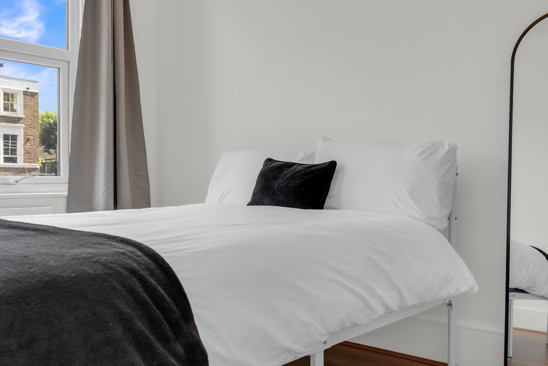 Bright bedroom with white bed, black accent pillow, window view of street, modern arc lamp