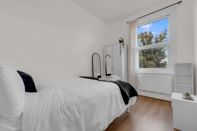 Bright bedroom with double bed, white bedding, wooden floor and large window with garden view