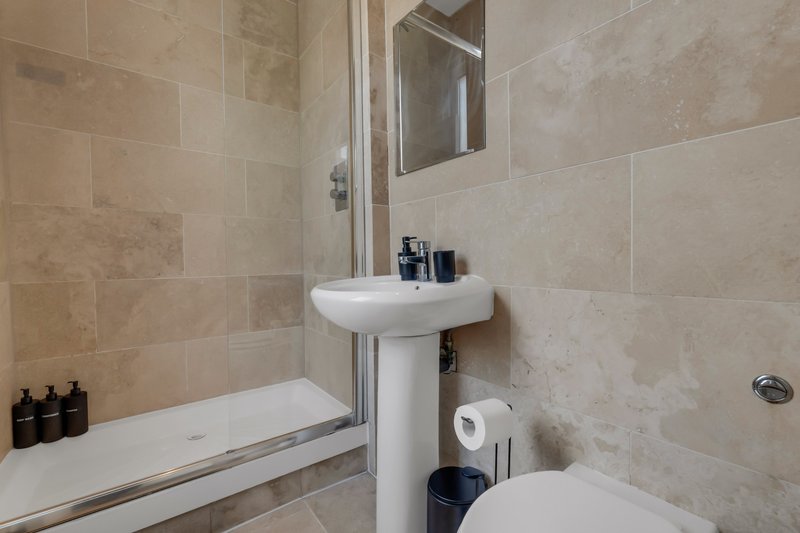 Modern bathroom with pedestal sink, shower enclosure, toilet and beige tile walls
