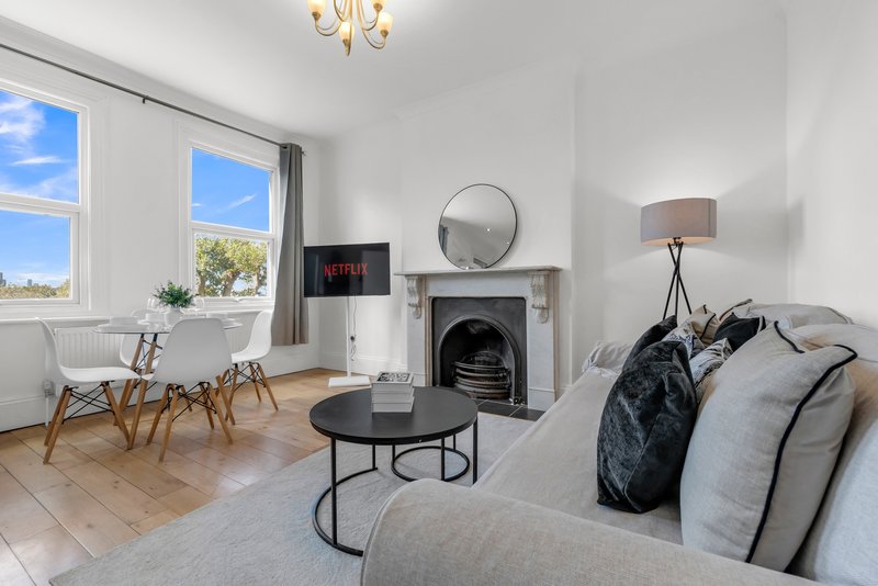 Bright living room with fireplace, grey sofa, round coffee table, and windows overlooking garden