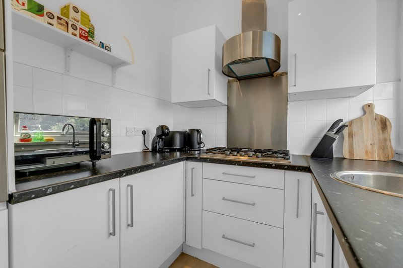 Modern white kitchen with black countertops, stainless steel appliances and range hood