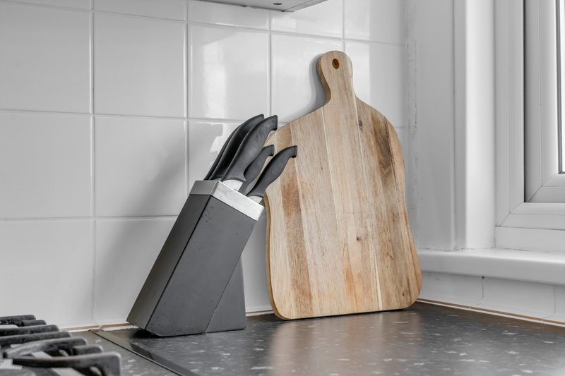 Modern kitchen counter with knife block, wooden cutting board and white tile backsplash