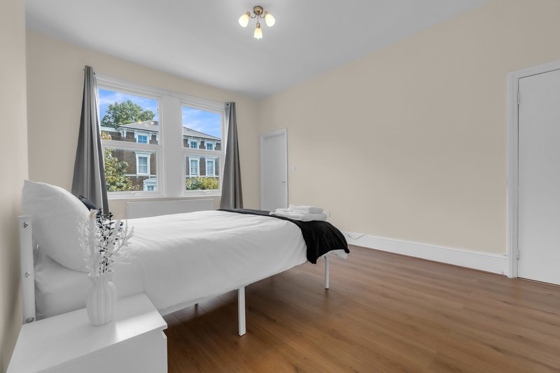 Bright bedroom with white bed, wooden floor, window with street view, and white doors