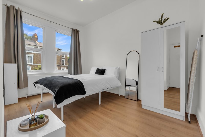 Bright bedroom with single bed, white wardrobe, wooden floor and large windows overlooking street