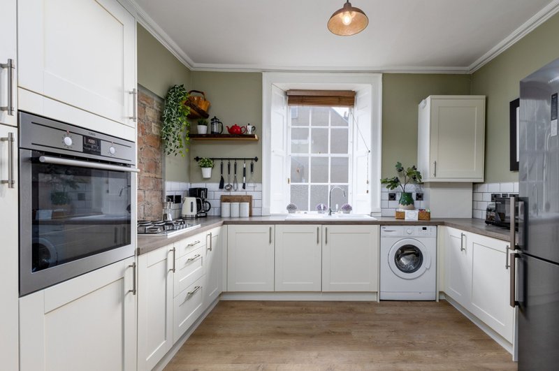 Modern kitchen with white cabinetry, integrated appliances, sage green walls and wooden flooring