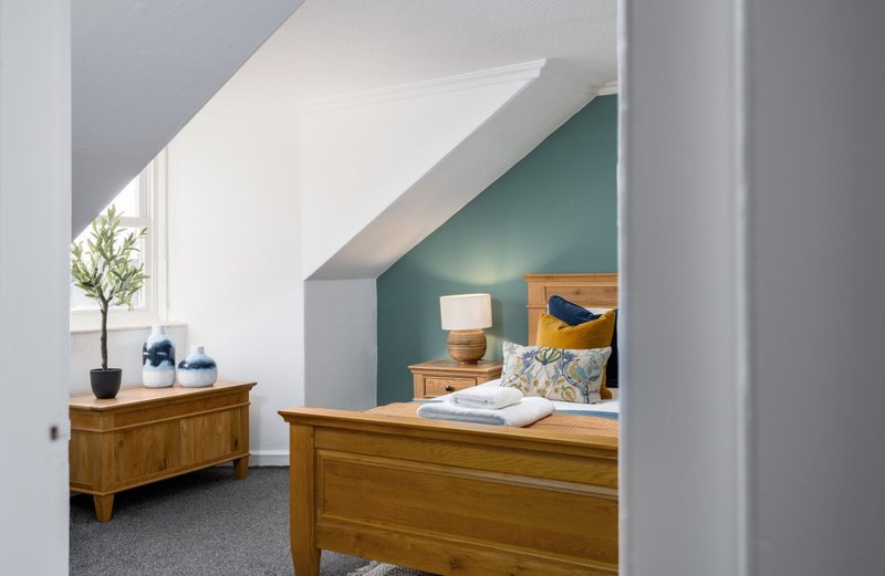 Attic bedroom with wooden furniture, teal accent wall, sloped ceiling and natural light
