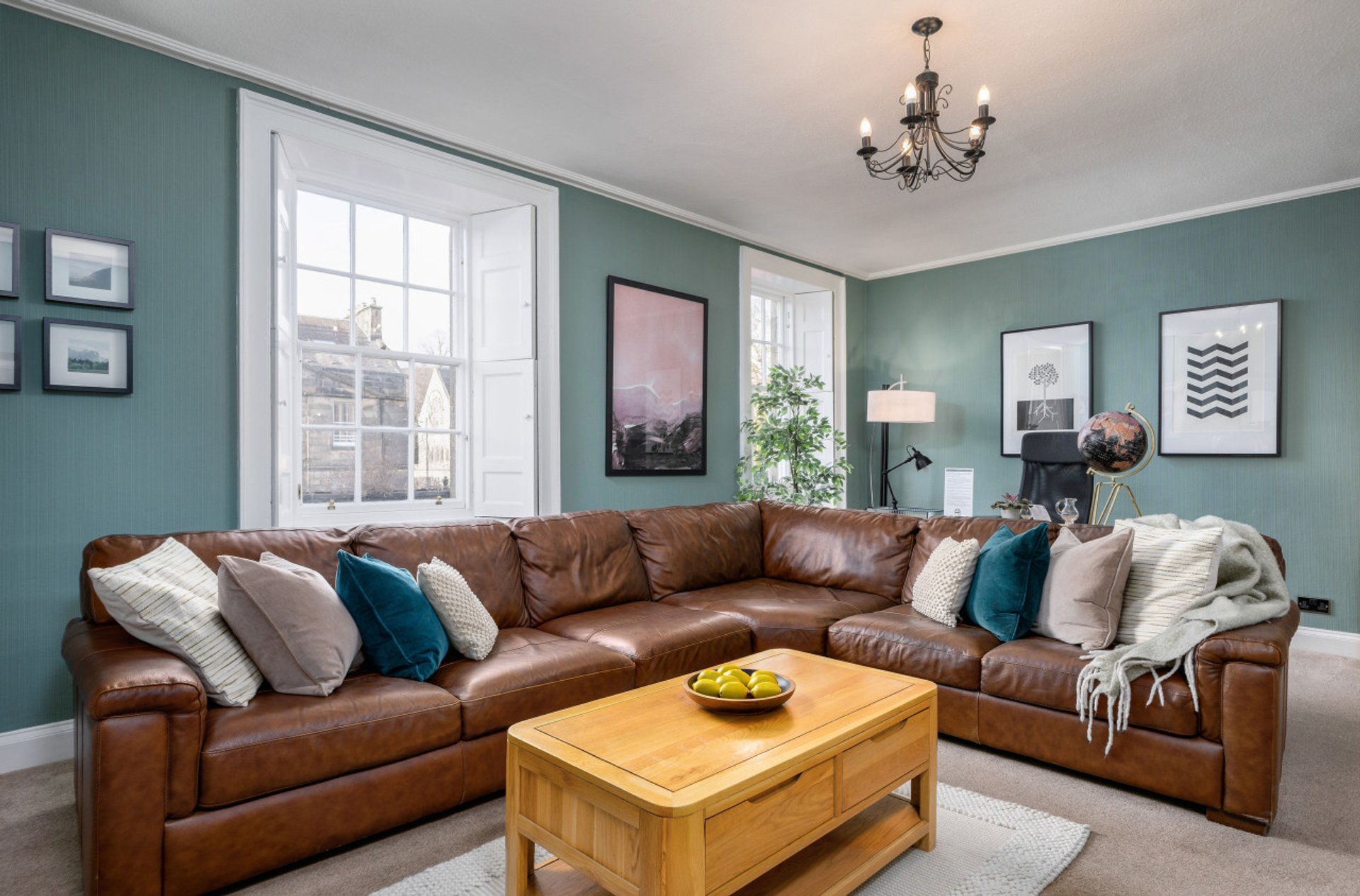 Modern living room with brown leather corner sofa, wooden coffee table, teal walls and framed artwork