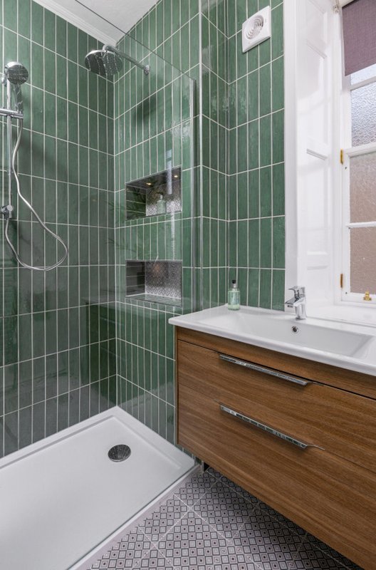 Modern bathroom with green subway tile walls, wooden vanity, white sink, and shower area