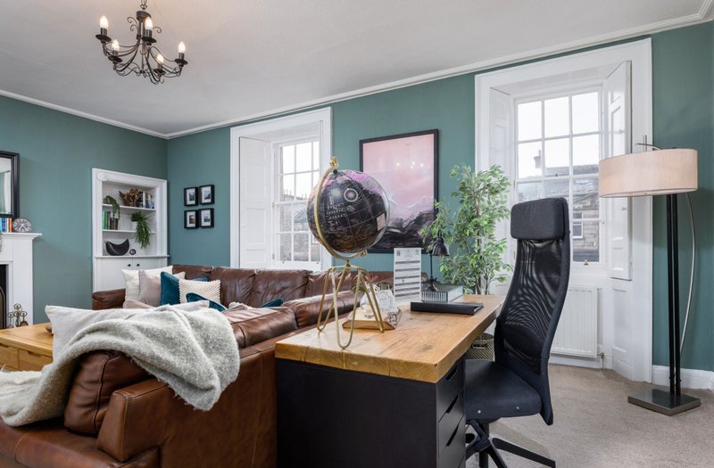 Spacious living room with teal walls, brown leather sofa, wooden table, globe, potted plant and floor lamp
