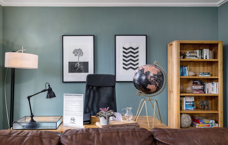 Styled desk area with framed wall art, globe, lamp, wooden bookshelf and brown upholstered seating