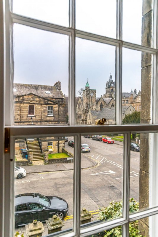 Window view of historic stone buildings, church spire and street with parked cars below