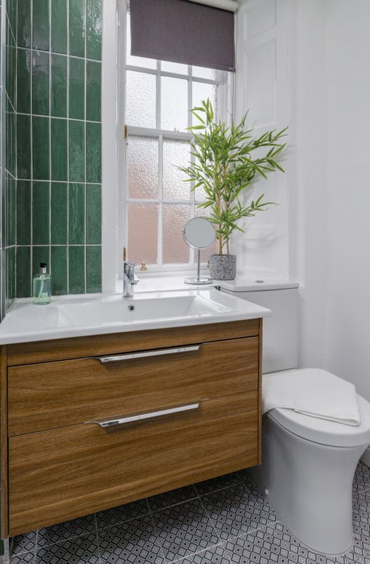 Modern bathroom with wooden vanity, white sink, toilet, window with blind and potted plant
