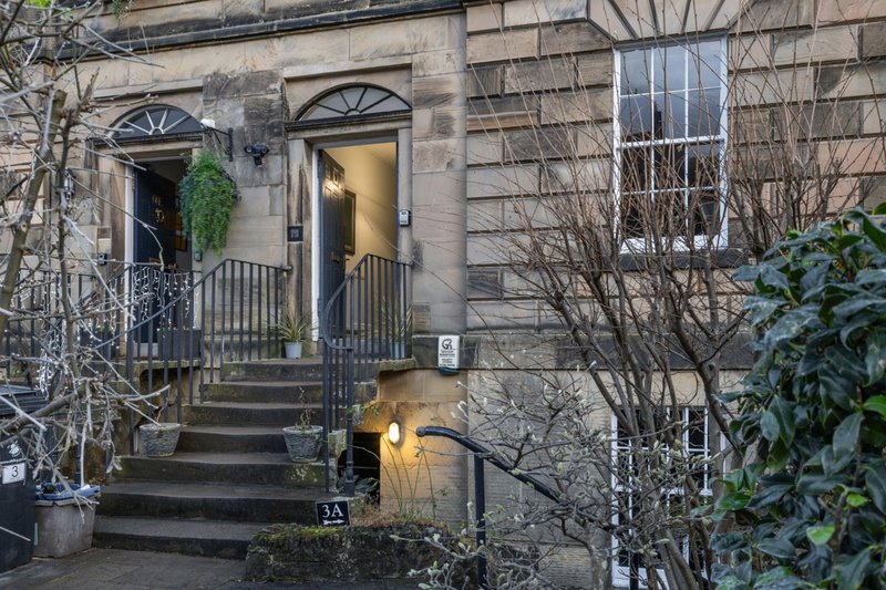 Stone townhouse exterior with dark door, lit entrance, railings, and bare climbing ivy