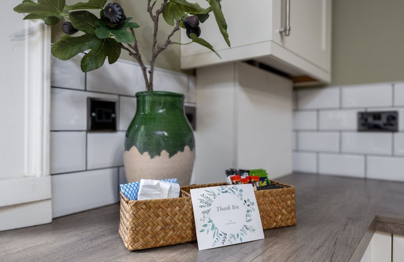 Kitchen counter with green vase, potted plant, woven baskets, and thank you card
