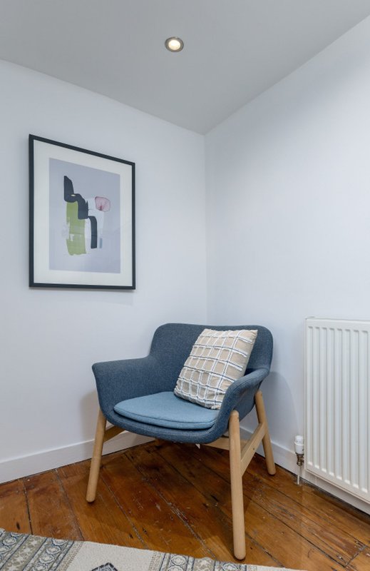 Modern bedroom corner with blue armchair, framed abstract wall art, wooden floor and radiator