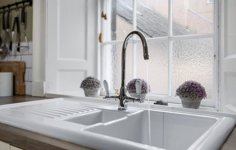 Kitchen sink with black tap, white countertop and windowsill with potted plants