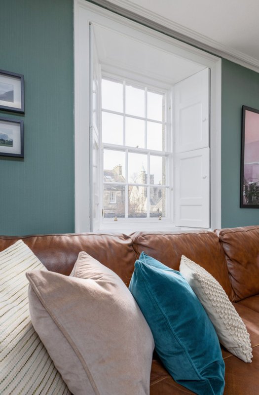 Living room with brown leather sofa, cushions, sash window and teal feature wall