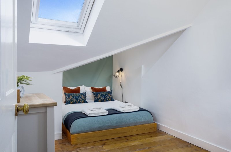 Bright attic bedroom with wooden bed, blue headboard, skylight window and sloped ceiling