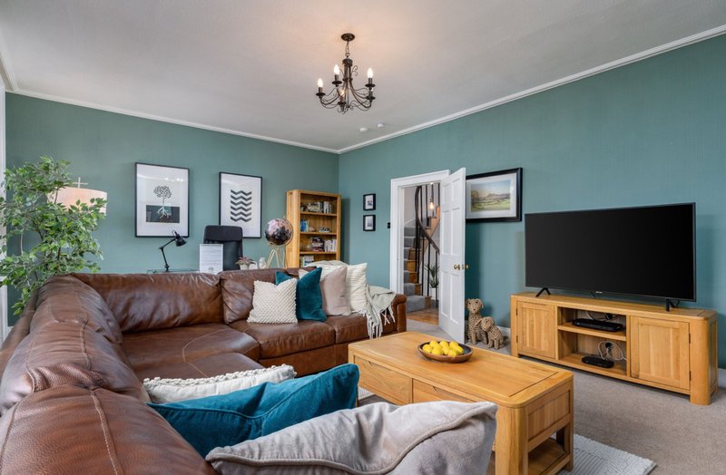 Turquoise living room with brown leather sofa, wooden TV stand, and framed wall art