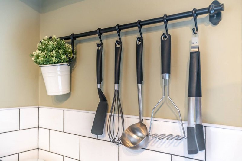 Kitchen wall with subway tile backsplash, black rail rod, hanging cooking utensils and potted plant