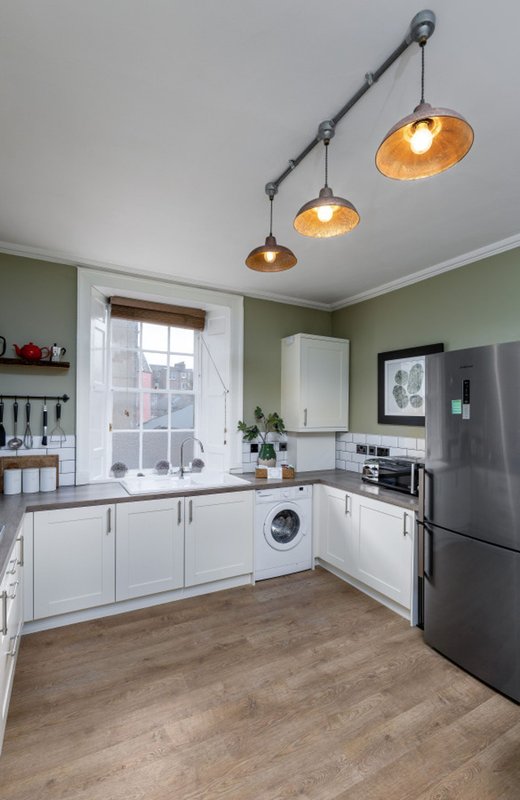 Modern kitchen with white cabinets, stainless steel appliances, pendant lights, and green walls