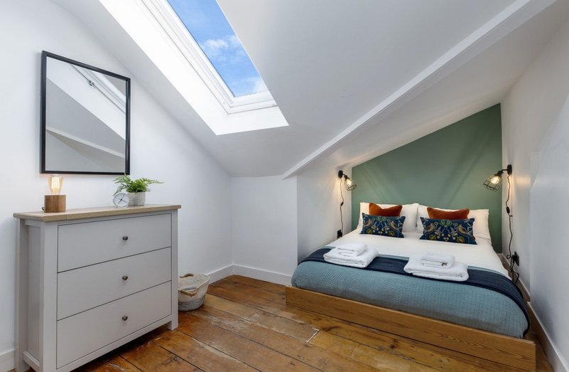 Bright attic bedroom with skylight, double bed, green headboard, wooden floor and chest of drawers