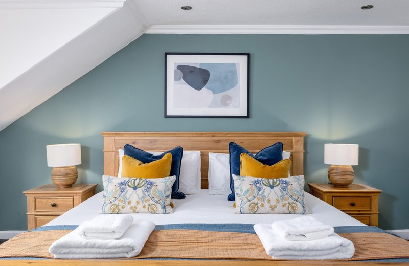 Bright bedroom with teal walls, wooden bed frame, decorative pillows and white towels