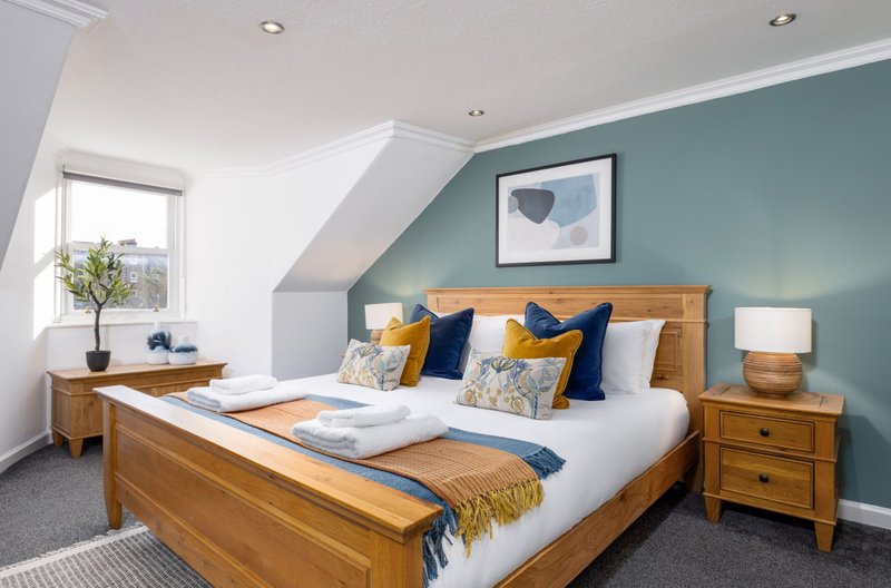 Modern bedroom with wooden bed, teal accent wall, white bedding, and window with natural light