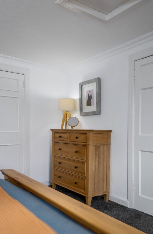 Bedroom corner with wooden dresser, brass lamp, framed artwork, and white doors
