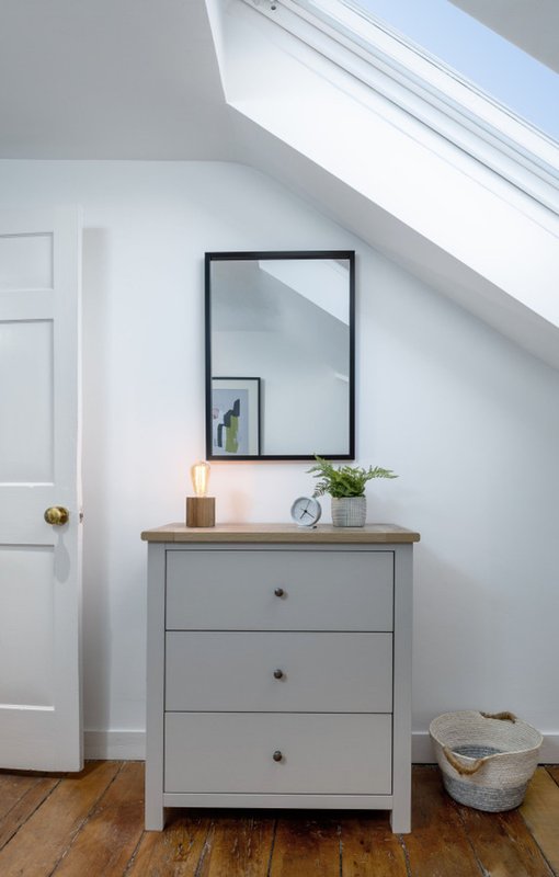 Bright attic bedroom corner with grey dresser, mirror, skylight window and wooden floor