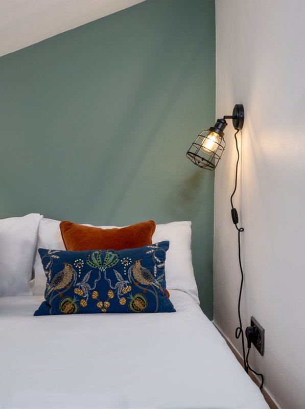 Bedroom with white bed, decorative pillows, green accent wall, and wall-mounted lamp