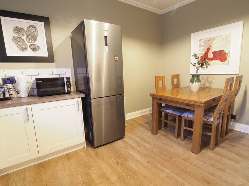 Open-plan kitchen and dining area with stainless steel fridge, wooden dining table, and framed wall art