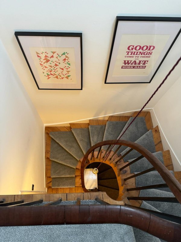 Spiral staircase with wooden treads, gray carpet, and framed wall art above