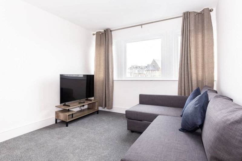 Modern living room with grey sofa, TV stand, window with curtains and street view