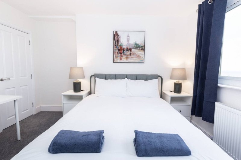 Bedroom with double bed, blue cushions, bedside lamps, framed wall art and blue curtains