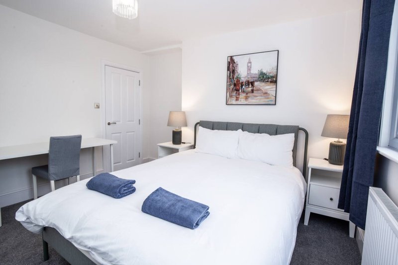 Bedroom with double bed, white bedding, two blue towels, bedside lamps and framed wall art