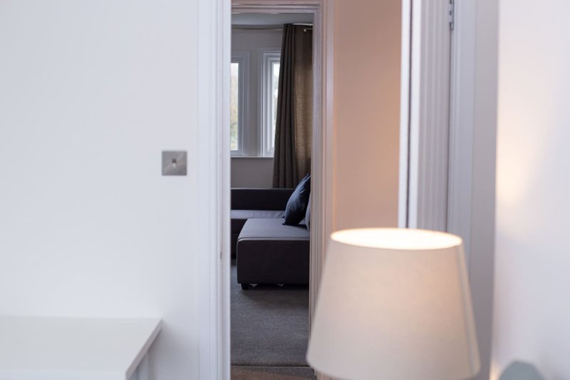 Modern hallway with white walls, open doorway leading to bedroom with dark furniture