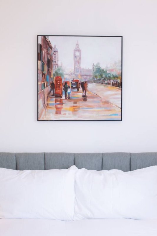 Bedroom with gray upholstered headboard, white pillows, and framed London street scene artwork
