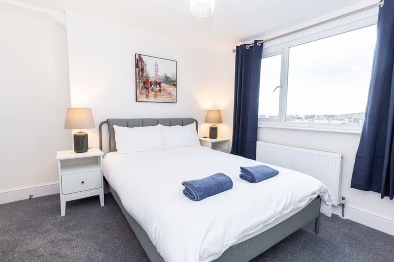 Bright bedroom with double bed, white bedding, grey headboard, matching nightstands and lamps