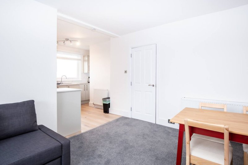 Studio apartment living area with grey sofa, kitchenette, wooden dining table and white door