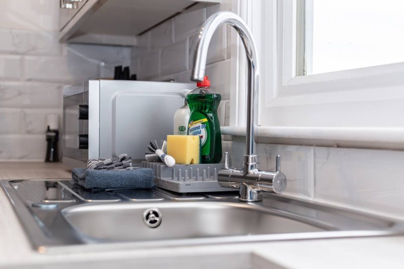Modern kitchen sink with chrome tap, cleaning supplies and dish rack