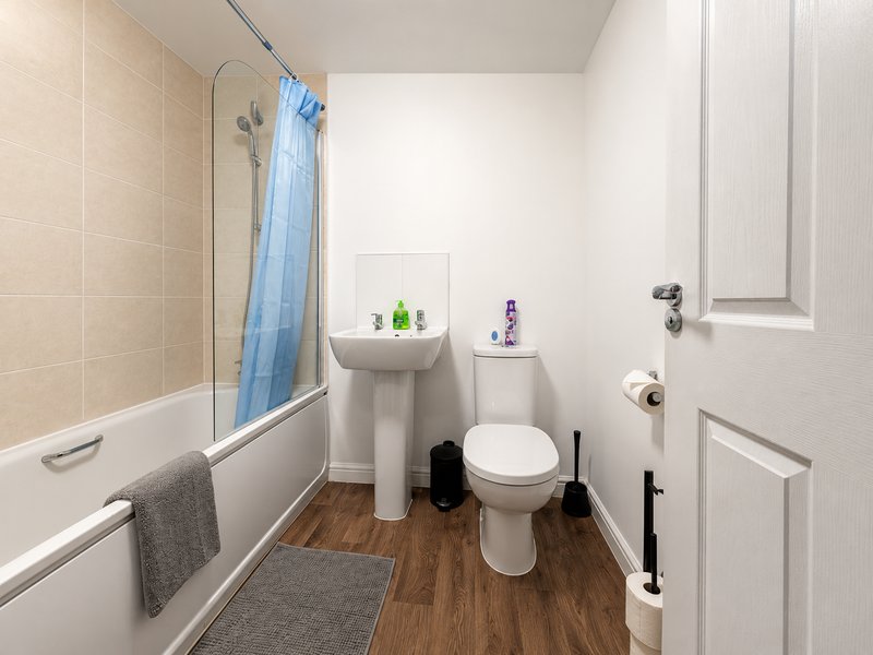 Bathroom with toilet, pedestal sink, bathtub with blue shower curtain and wooden flooring