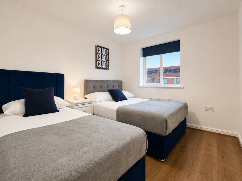 Bedroom with one single and one double bed, navy headboards, grey throws, pendant light and window