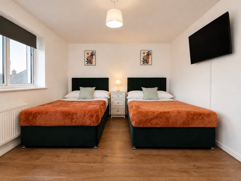 Twin bedroom with two double beds, orange throws, green headboards, wall-mounted TV, bedside lamp and wall art and window