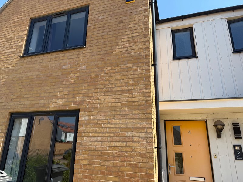 Exterior view of two-storey brick house with adjacent modern cladding property and orange door