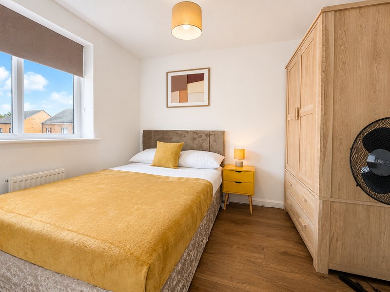 Bright bedroom with double bed, yellow bedding, wooden wardrobe and window view