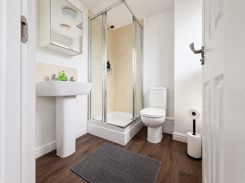 Clean modern bathroom with corner shower enclosure, pedestal sink, toilet and wooden flooring