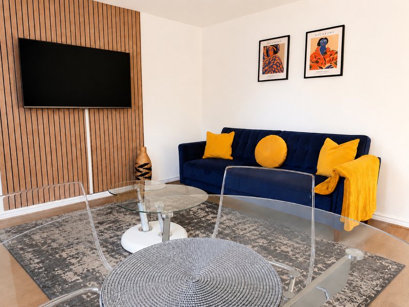 Modern living room with navy sofa, yellow cushions, wall-mounted TV, framed wall art and round coffee table