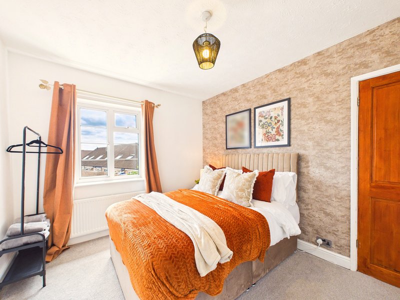 Bright bedroom with double bed, orange bedding, brick accent wall, and window with countryside view
