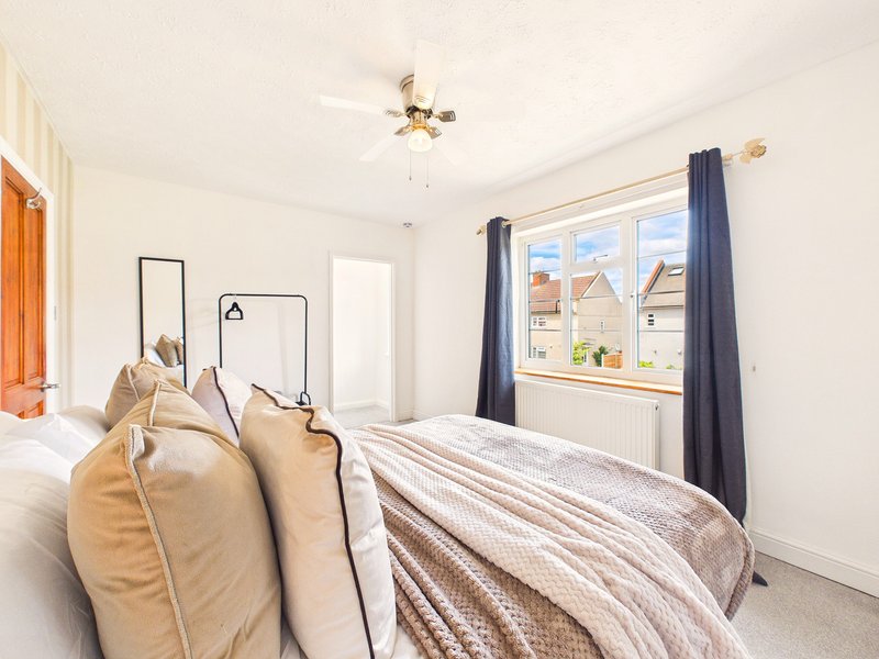Bright bedroom with double bed, cushions, window with blue curtains and residential view